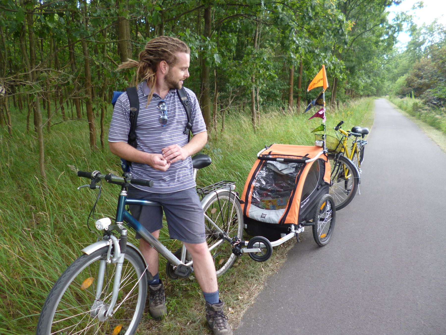 Adam with a child bike trailer, on a tree-lined path in Berlin.