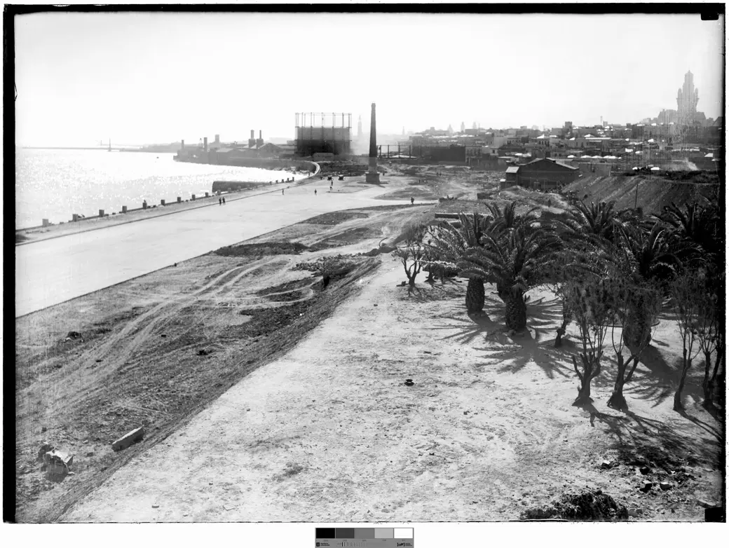 Historical photo, 1928–1935: the Rambla Sur under construction at Rambla Argentina and Cuareim streets, with the Dique Mauá and the gasworks chimney behind.