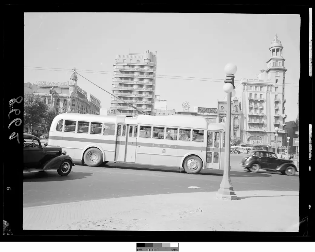 A trolleybus lettered AMDET and showing route 62 runs along Calle Colonia among period cars, under the overhead wires; tall buildings behind, and a street lamp in the foreground.