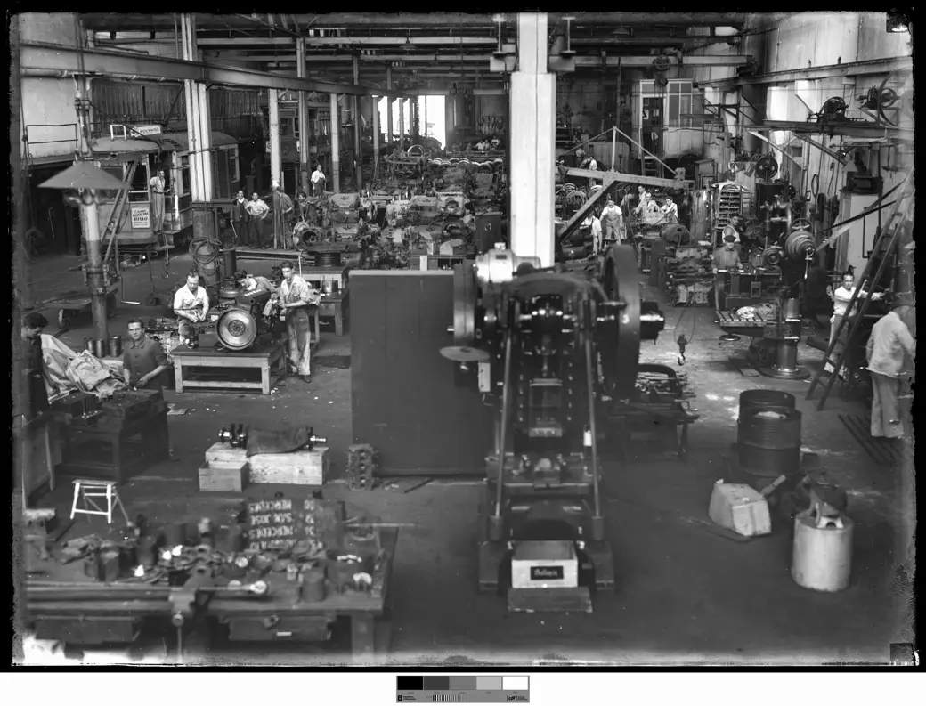 A workshop floor seen from above: lathes, presses and workbenches with workers, and a tramcar at the back on the left.