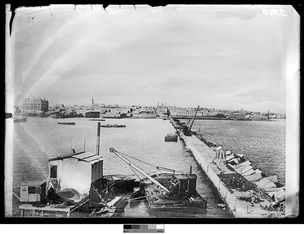 Historical photo, 1901-1903: the Sarandí breakwater under construction, a floating platform with cranes, stone blocks laid in a line, the Hotel Nacional and Ciudad Vieja on the horizon.