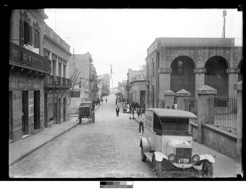 Historical photo, circa 1920: Calle Yerbal, with a delivery truck, a horse carriage, and pedestrians walking down the middle of the road.