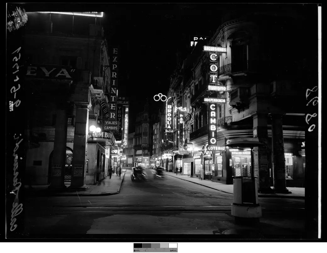 Historical photo, 9 May 1951: Sarandí at Juncal at night, with neon signage and a car in motion down the roadway.